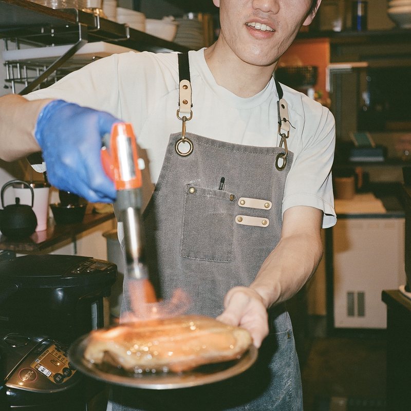 Chef torching a piece of fish in a restaurant kitchen